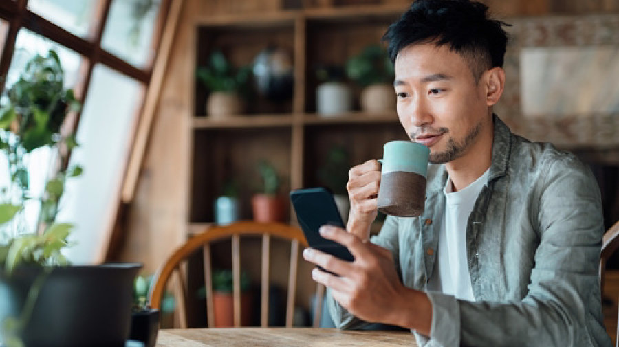 a man sips from a mug as he reviews something on his smartphone