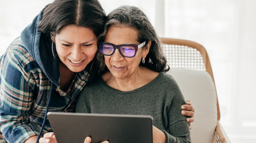 an older mother and her adult daughter cheerfully inspecting something on a tablet computer