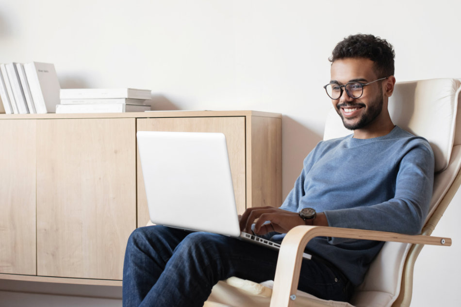 cheerful man sits back in a chair as he works on his laptop computer